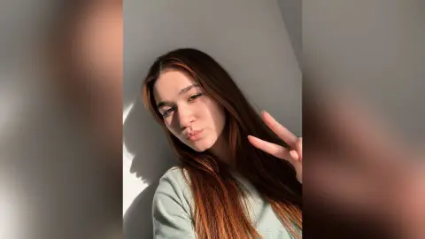 JaneBarbrick poses with a peace sign, looking at the camera with long brown hair and a light green shirt.