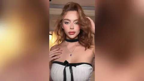 Glamorous woman in a white strapless top and black choker posing with soft, elegant makeup in a warm setting.