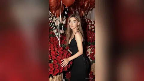 Elegant woman in a black evening dress posing amidst red roses and copper balloons for a romantic celebration.
