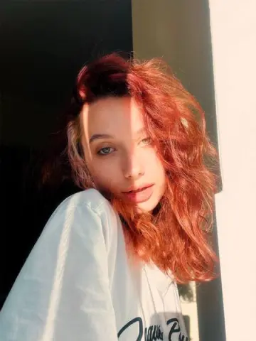Young woman with wavy red hair wearing a white t-shirt in warm, cinematic sunlight.