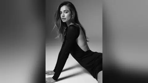 Elegant woman in a black long-sleeve backless dress posing in a moody black and white studio portrait.