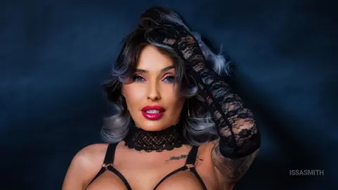 Glamorous woman in black lace lingerie and choker posing against a dark moody background.