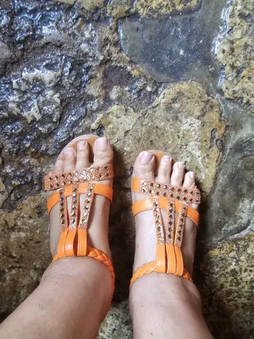 Close-up of feet wearing sparkly orange strappy sandals on a rustic stone floor.