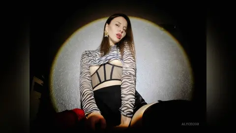 Young woman in a striped sheer top and black skirt posing under dramatic spotlight in a moody setting.