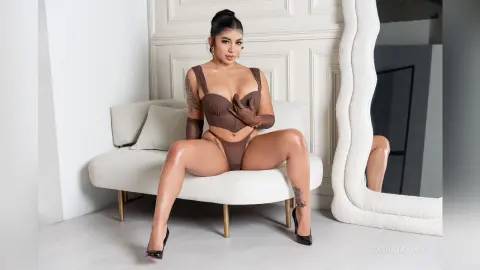 Curvy woman in brown lingerie and gloves sitting on a white sofa in a bright, modern minimalist room.