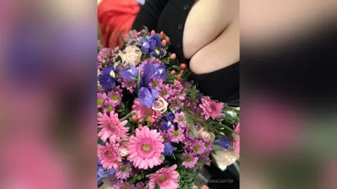 Woman in a black top holding a vibrant bouquet of pink and purple flowers in a soft, romantic setting.