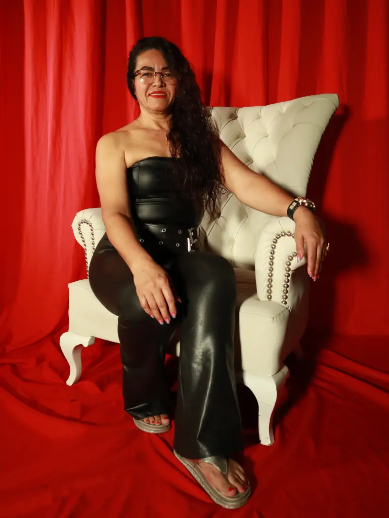 MatureePure poses sitting in a white chair wearing a black strapless leather outfit with her long dark hair down.