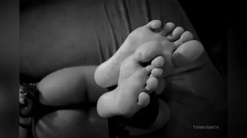 TannySmith lies on a bed, showing her bare feet and soles in a close-up black and white shot.