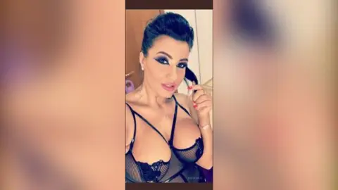 MissyJolie poses in black sheer lingerie with thin straps, looking at the camera with heavy eye makeup and dark hair pulled back.