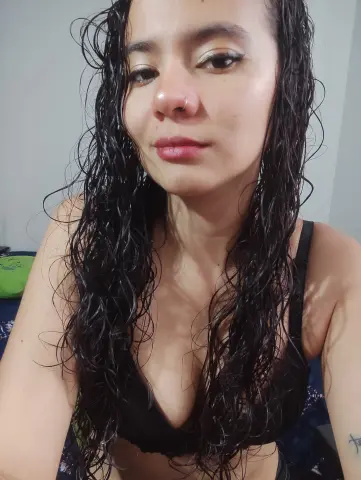 Young woman with wet curly hair wearing a black bikini top in a bright indoor setting.