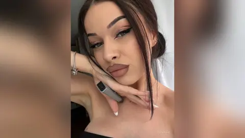 AriaVex poses with her hands near her face, showing off her long dark hair and heavy winged eyeliner.
