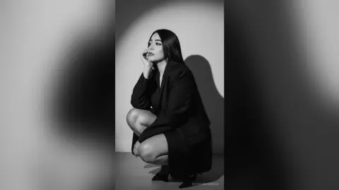 Elegant woman in a black blazer posing thoughtfully in a minimalist black and white studio setting.