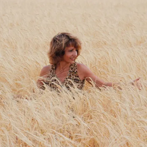 Smiling woman in a leopard print top relaxing in a golden wheat field during a sunny summer day.