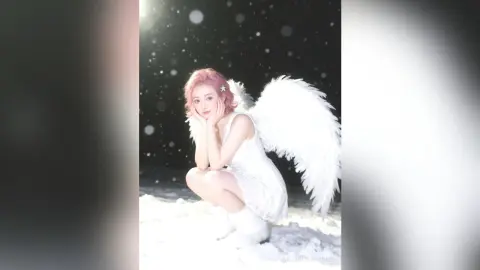Dreamy girl with pink hair in a white angel costume sitting in a snowy winter wonderland.