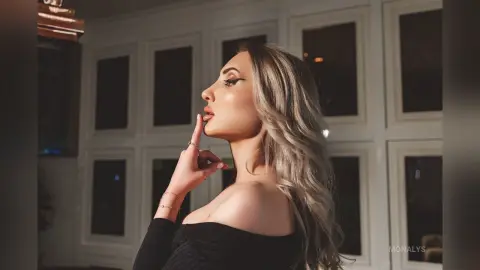 Glamorous woman with silver hair in a black off-the-shoulder top posing elegantly against a window backdrop.