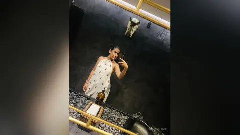 Woman in a white halter dress taking a mirror selfie in a moody, dark modern bathroom.