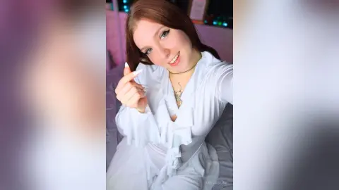 Smiling young woman in a white ruffled blouse posing in a bright, cozy indoor setting.