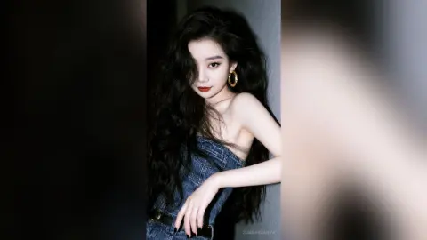 Elegant woman with long wavy black hair wearing a denim strapless top in a moody studio setting.