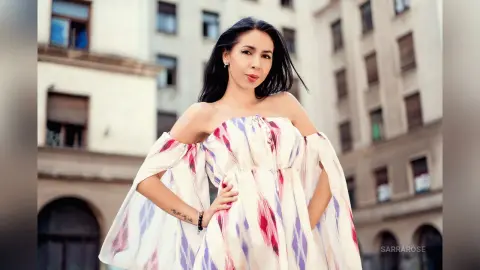 Young woman in a white and purple off-the-shoulder floral dress posing in a city street setting.