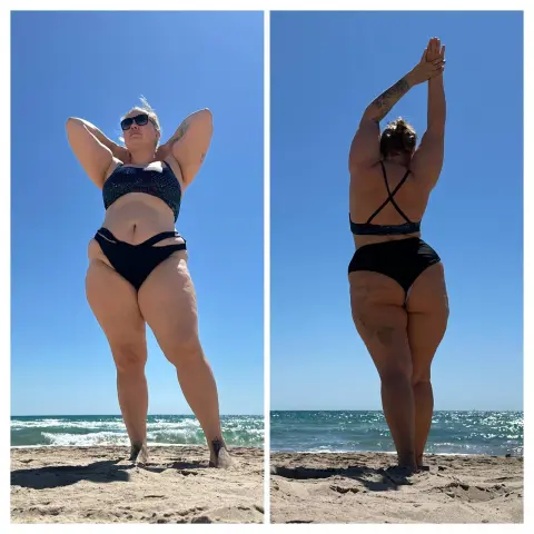 Curvy woman in a black bikini posing on a sunny beach under a clear blue sky.