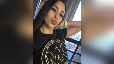 Young woman in a black Michael Kors t-shirt making a playful pout by a city view window.