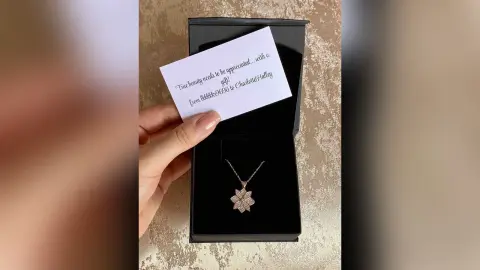 Hand holding a handwritten gift note above an open black jewelry box containing a sparkling star pendant necklace.