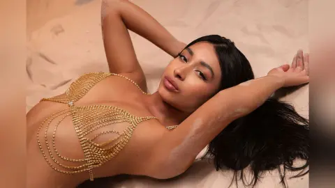 Beautiful woman in a gold chain bikini lying on sand for a glamorous summer beach photoshoot.