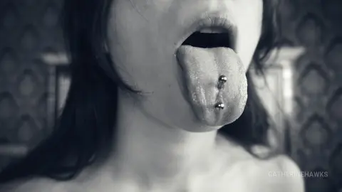 Close-up black and white portrait of a woman with a silver tongue piercing sticking her tongue out.