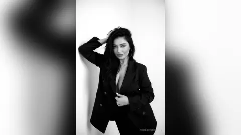Elegant woman in a black blazer posing against a white wall in a moody black and white portrait.