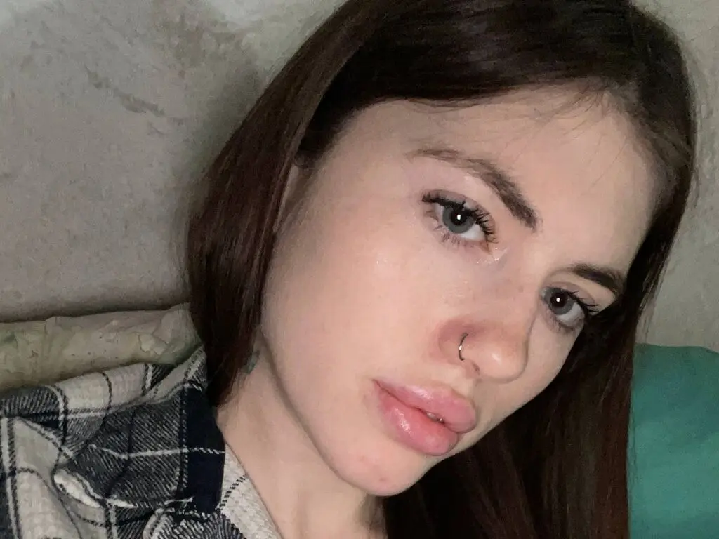 MitsueEastes looks directly at the camera with long brown hair and a nose ring, wearing a dark plaid shirt.