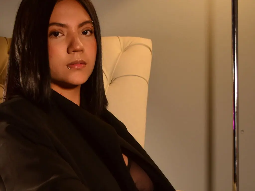 Moody portrait of a woman with dark hair wearing a black outfit sitting in a beige armchair.