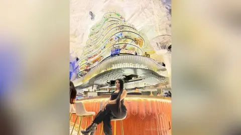 Stylish woman in black outfit sitting at a modern luxury bar with glowing amber lighting and designer decor.