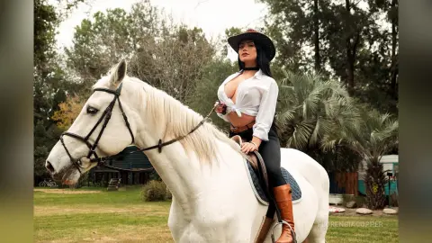 FlorenciaCopper sits upright on a white horse wearing a white button-down shirt and black leggings in an outdoor setting.