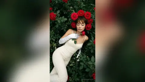 SophiaNapoles poses in a white dress and white gloves, surrounded by red roses and green leaves.