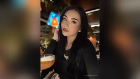 Young woman with long dark hair in a black top enjoying a cocktail in a dimly lit restaurant setting.
