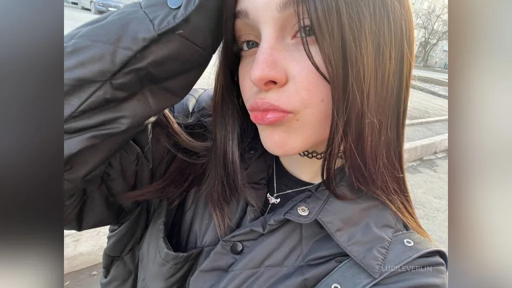 LucileVerlin — LucileVerlin poses outdoors in a black puffer jacket with her hand in her hair.