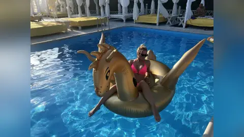 MilenaBia floats in a swimming pool wearing a pink bikini while sitting on a large gold inflatable dragon float.