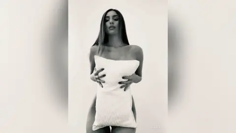 Young woman in white strapless loungewear holding a pillow against a minimalist white background.