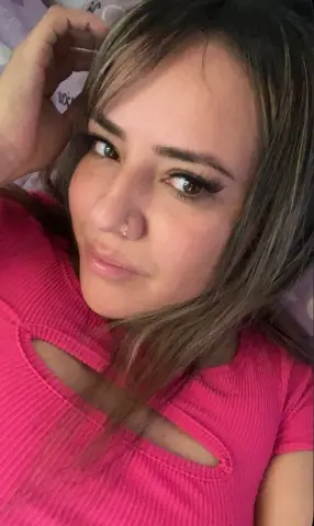 Young woman with long brown hair wearing a pink ribbed top relaxing in a cozy indoor setting.