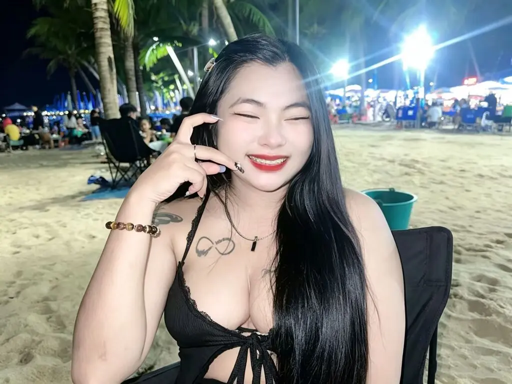 Smiling woman in a black bikini sitting on a tropical beach at night under palm trees.