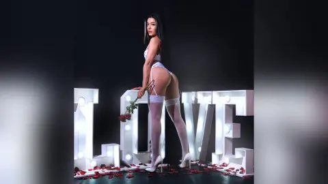 JessieLiu poses sideways behind large white light-up letters, wearing white lace lingerie and white thigh-high stockings while holding a red rose.