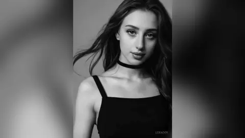 Portrait of a beautiful young woman with long wavy hair wearing a black tank top and choker in a moody setting.