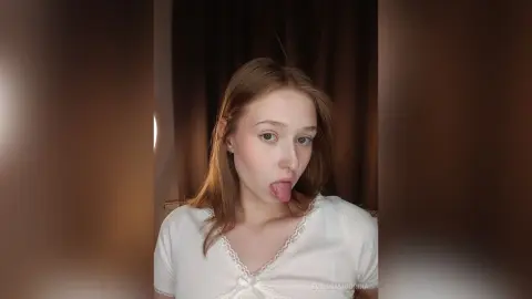 Young woman in a white lace camisole making a playful expression in a dimly lit room.