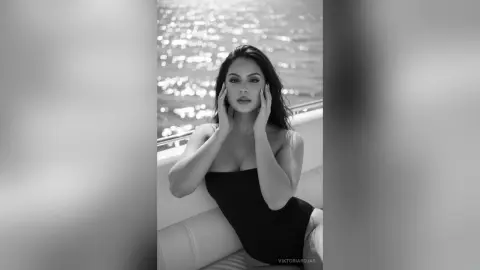 Elegant woman in a black dress sitting on a boat against a sparkling ocean background in a moody black and white portrait.
