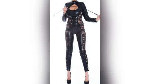 KateRichman stands in a black lace and leather bodysuit, pulling at the neck or straps against a white background.