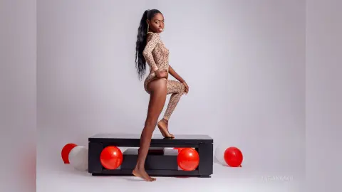 Elegant Black woman in a patterned bodysuit posing on a black bench with red and white balloons.