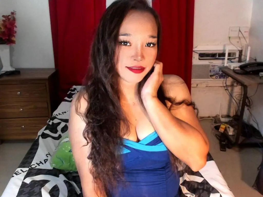 Young woman with long wavy hair in a blue dress relaxing in a bedroom setting.