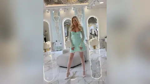 Elegant woman in a mint green mini dress posing in a luxurious marble ballroom with classical decor.