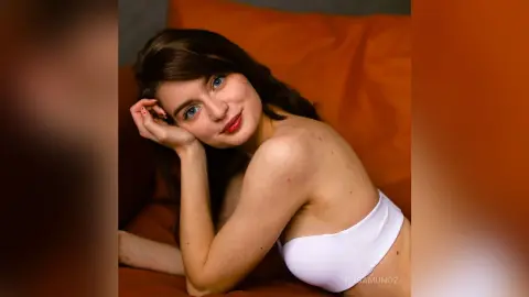 Young woman in white lingerie relaxing on an orange sofa with a peaceful expression.