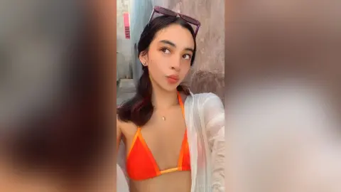 Young woman in an orange bikini and white cover-up posing outdoors with a relaxed summer mood.